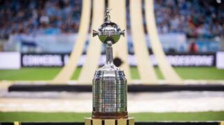 Taça da Libertadores no gramado, com símbolo da competição ao fundo