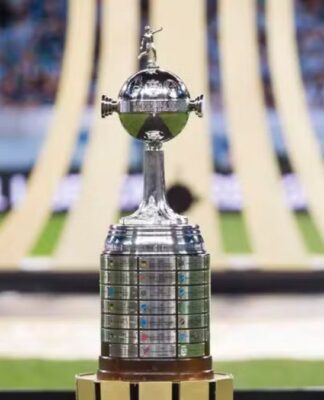 Taça da Libertadores no gramado, com símbolo da competição ao fundo