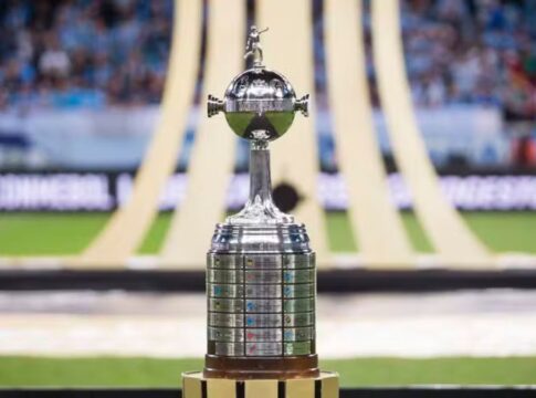 Taça da Libertadores no gramado, com símbolo da competição ao fundo