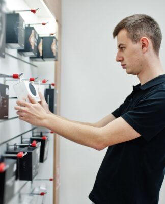 Homem branco e loiro de camiseta preta analisando produtos a venda em uma loja de eletrônicos