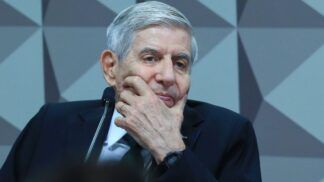 O general Augusto Heleno apoia o rosto com a mão enquanto participa de sessão no Congresso, diante do microfone