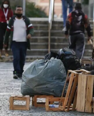 Mulher em situação de rua limpa a entrada de sua barraca