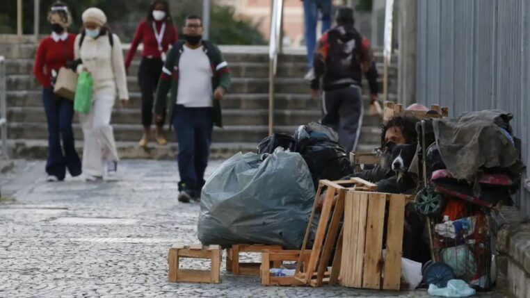 Mulher em situação de rua limpa a entrada de sua barraca