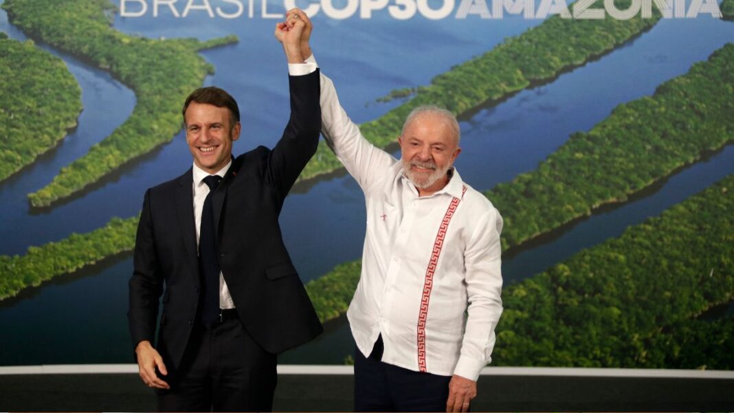 Presidente Lula sorri e levanta o braço do presidente francês, Emmanuel Macron, em gesto de vitória