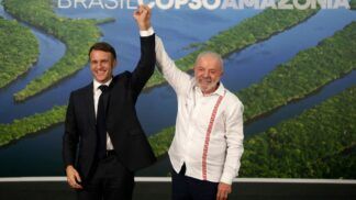 Presidente Lula sorri e levanta o braço do presidente francês, Emmanuel Macron, em gesto de vitória