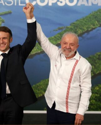Presidente Lula sorri e levanta o braço do presidente francês, Emmanuel Macron, em gesto de vitória