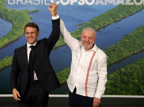 Presidente Lula sorri e levanta o braço do presidente francês, Emmanuel Macron, em gesto de vitória