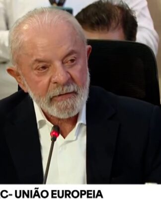 Lula, sentado de terno azul marinho e camisa branca, discursando