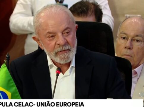 Lula, sentado de terno azul marinho e camisa branca, discursando