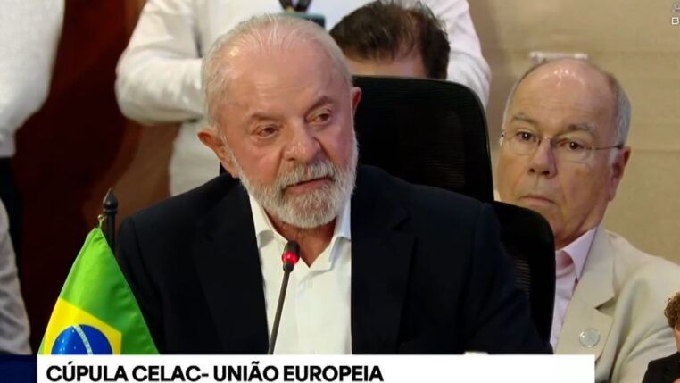 Lula, sentado de terno azul marinho e camisa branca, discursando