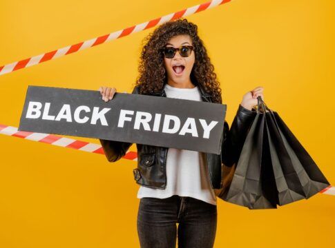 Mulher em fundo amarelo, segurando sacolas pretas e placa escrita black friday