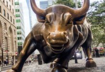 O ChatGPT disse: Escultura do Touro de Wall Street em Nova York, símbolo de força e otimismo do mercado financeiro, vista de frente em uma rua cercada por prédios e pedestres.