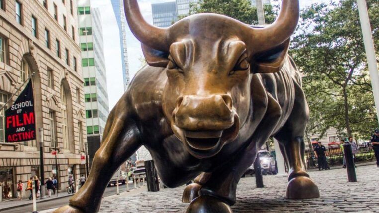 O ChatGPT disse: Escultura do Touro de Wall Street em Nova York, símbolo de força e otimismo do mercado financeiro, vista de frente em uma rua cercada por prédios e pedestres.
