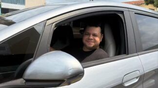 Motorista Alberto dentro de um carro prata, no banco do motorista