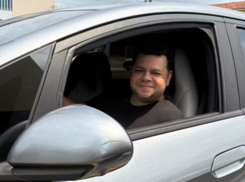 Motorista Alberto dentro de um carro prata, no banco do motorista