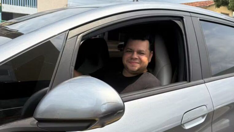Motorista Alberto dentro de um carro prata, no banco do motorista