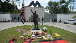 Entrada do CT Ninho do Urubu com faixas, flores e bandeiras do Flamengo em homenagem aos mortos