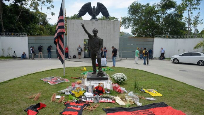 Entrada do CT Ninho do Urubu com faixas, flores e bandeiras do Flamengo em homenagem aos mortos