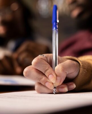 Mão de mulher negra segurando uma caneta azul e redigindo um texto