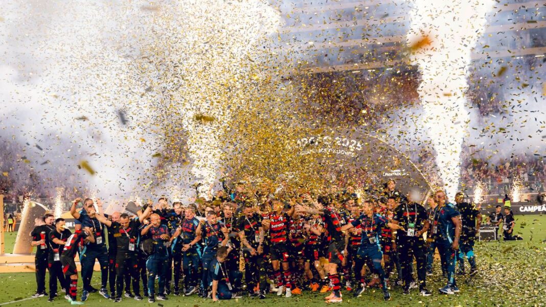 Jogadores do Flamengo festejam o tetracampeonato da Libertadores em meio a chuva de papel picado no gramado.