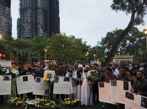 Dezenas de chineses carregam cartazes e flores com o prédio incendiado ao fundo