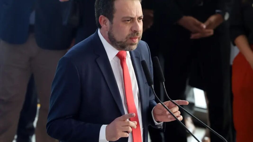 Boulos discursando em um palanque usa ndo terno escuro, camisa branca e gravata vermelha