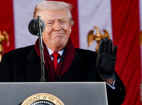 Donald Trump sorri diante de microfone com a bandeira dos EUA ao fundo