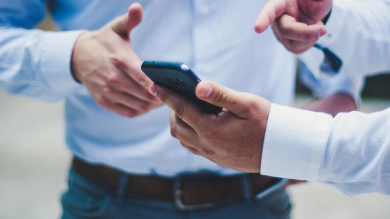 Uma mão segura um celular enquanto outra mão aponta para o aparelho