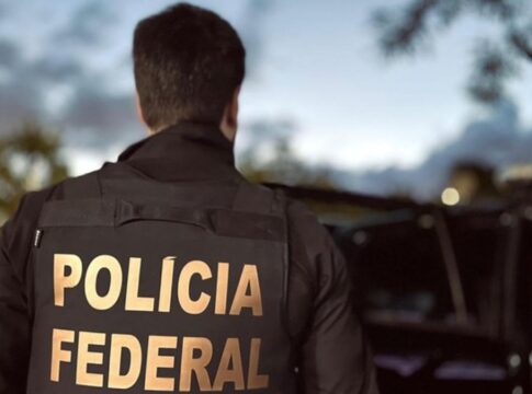 Agente, de costas, apresenta a inscrição polícia federal em seu uniforme