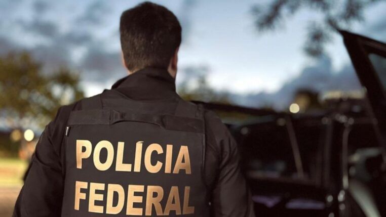 Agente, de costas, apresenta a inscrição polícia federal em seu uniforme