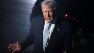 Trump gesticula após desembarcar de avião, à noite.