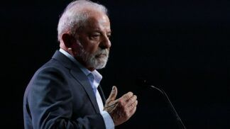 Lula faz gesto com a mão direita enquanto faz declaração ao microfone