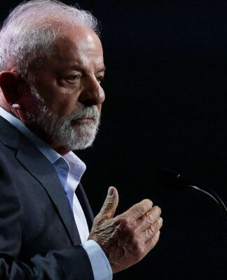 Lula faz gesto com a mão direita enquanto faz declaração ao microfone