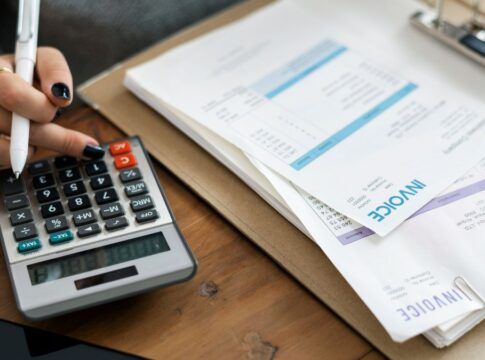 Mulher usa calculadora entre diversas contas sobre a mesa