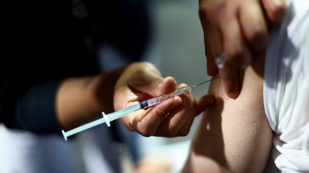 Close de uma seringa de vacinação aplicada no braço de uma pessoa