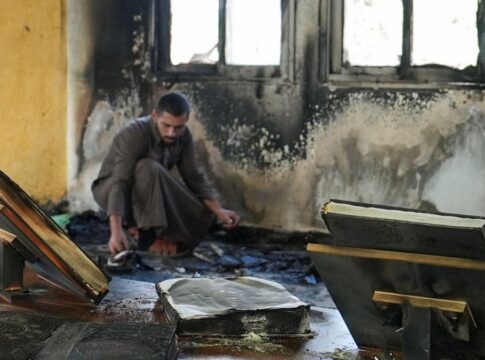 Homem dentro de uma mesquita com as paredes danificadas por chamas