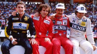 Ayrton Senna, Alain Prost, Nigel Mansell e Nelson Piquet estão sentados numa mureta com seus macacões durante um GP