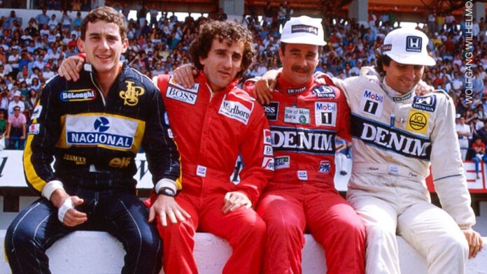 Ayrton Senna, Alain Prost, Nigel Mansell e Nelson Piquet estão sentados numa mureta com seus macacões durante um GP