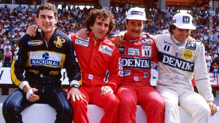 Ayrton Senna, Alain Prost, Nigel Mansell e Nelson Piquet estão sentados numa mureta com seus macacões durante um GP