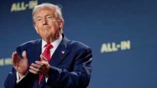 Trump aplaude com expressão de ironia à frente de um fundo azul