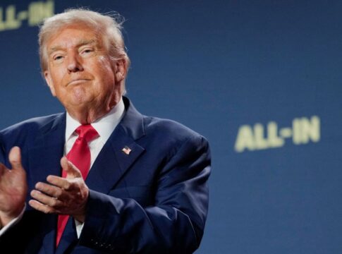 Trump aplaude com expressão de ironia à frente de um fundo azul