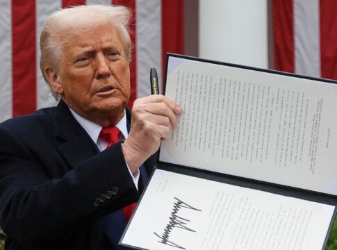 Donald Trump segura uma caneta com a mão direita e ergue texto de lei que assinou