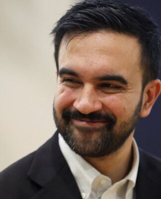 Zohran Mamdani de blazer escuro e camisa branca, sorrindo