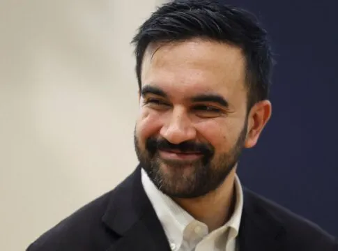 Zohran Mamdani de blazer escuro e camisa branca, sorrindo