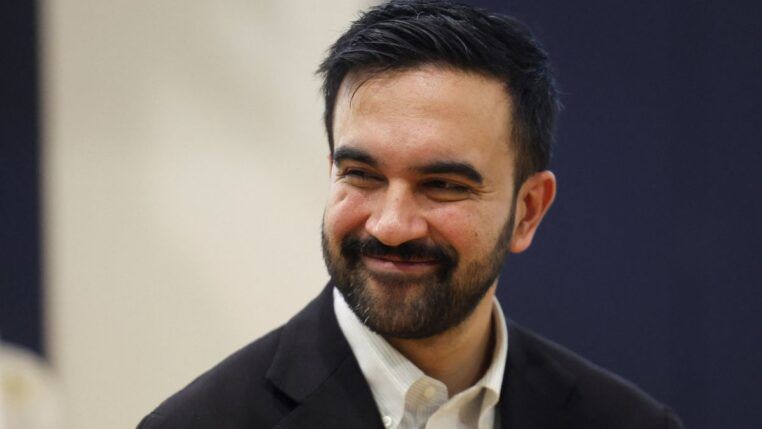 Zohran Mamdani de blazer escuro e camisa branca, sorrindo