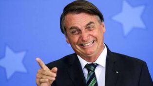 Foto antiga de Jair Bolsonaro, quando ainda era presidente, sorrindo e apontando com o dedo para fora da câmera