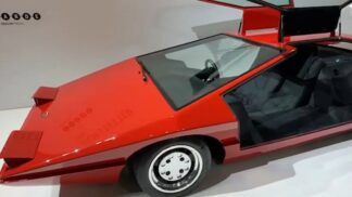 Foto de um carro esportivo vermelho de 1980, com bancos pretos e rodas de cor prateada