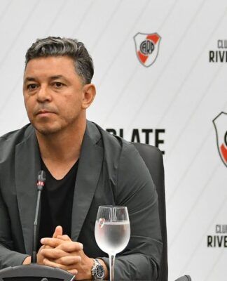 Técnico Gallardo, do River Plate, sentado com um copo de água ao seu lado, durante o anúncio de sua renovação de contrato