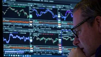 Homem de óculos, ao canto da imagem, analisando uma série de gráficos indicativos de bolsa de valores