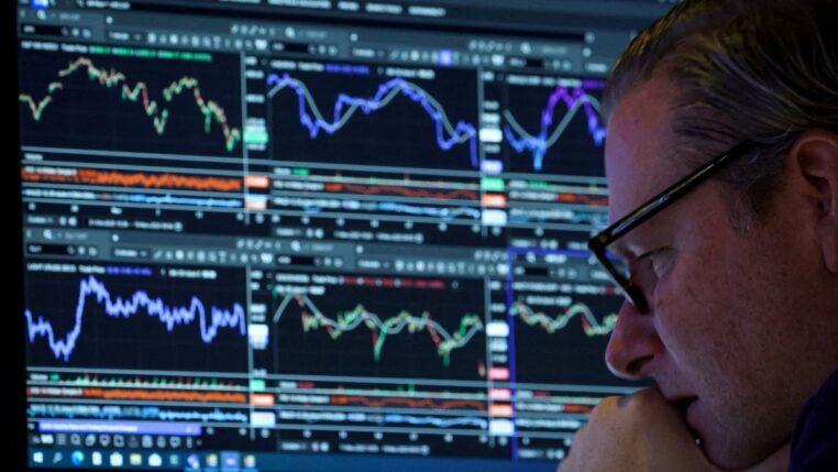 Homem de óculos, ao canto da imagem, analisando uma série de gráficos indicativos de bolsa de valores